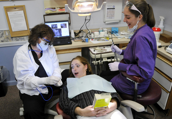 Adriane Williams of Portland reacts as Dr. Denise Theriault, left, shows her a wisdom tooth that was pulled during her visit Friday to Dunstan Dental Center in Scarborough, one of several offices in southern Maine that offered free dental care for the day. At right is hygienist Stephanie Fortier.