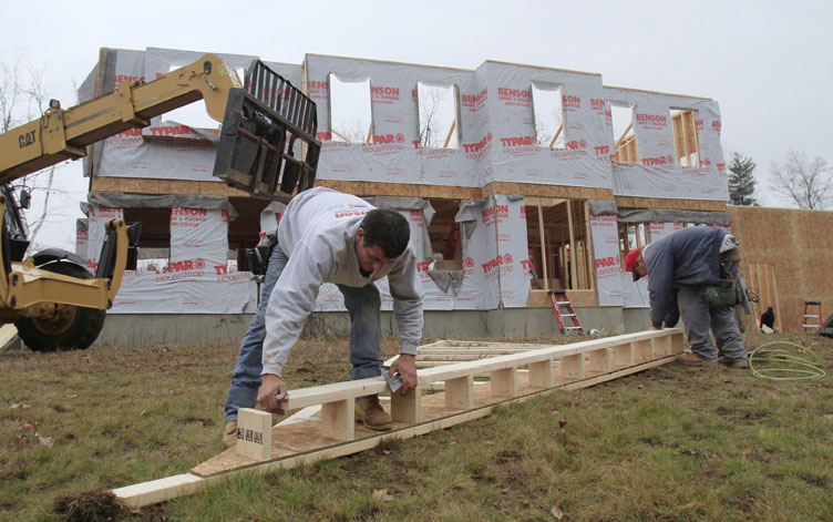 Builders nail together a roof panel for a home under construction in Derry, N.H. Home prices are falling faster in the nation's largest cities, and a record number of foreclosures are expected to push prices down further through next year.