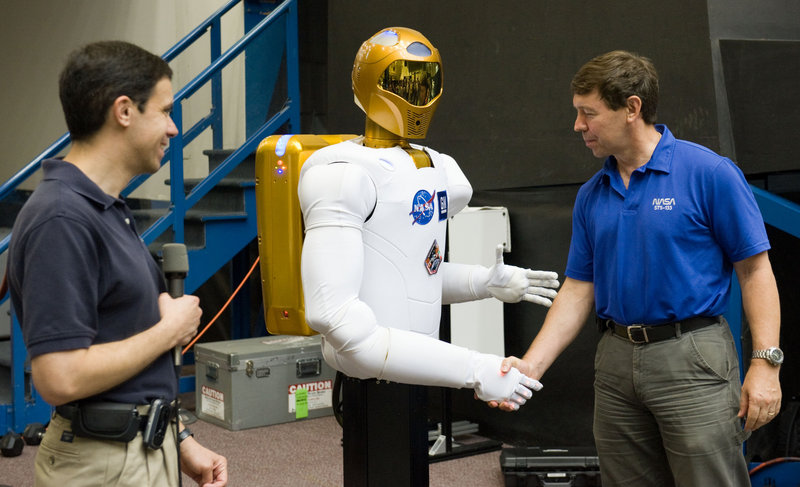 NASA astronaut Michael Barratt shakes hands with Robonaut 2 during a news conference in the Space Vehicle Mock-up Facility at the Johnson Space Center in Houston.