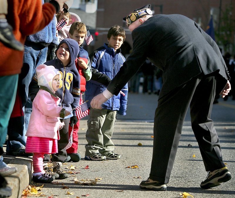 Veteran Mert Rutherford of Cape Elizabeth hands a small American flag to Carmelina Peterson, 2, of Portland during the Veterans Day parade in this 2009 file photo.