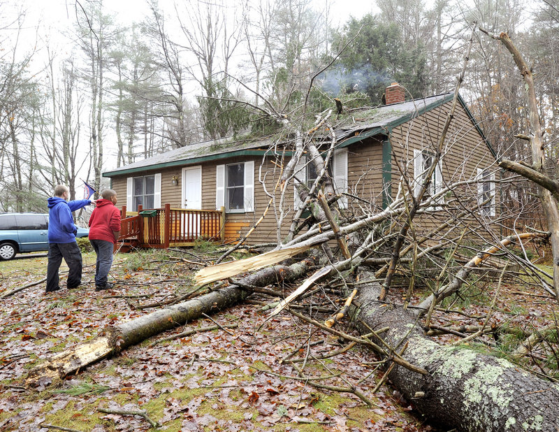 Logan Hillruel, 9, in red, shows his neighbor Dylan Weymouth, 12, the damage done by a large pine tree that fell on his home on Maine Road in New Gloucester during a windy rainstorm Monday. They were waiting for help to arrive and remove the tree.