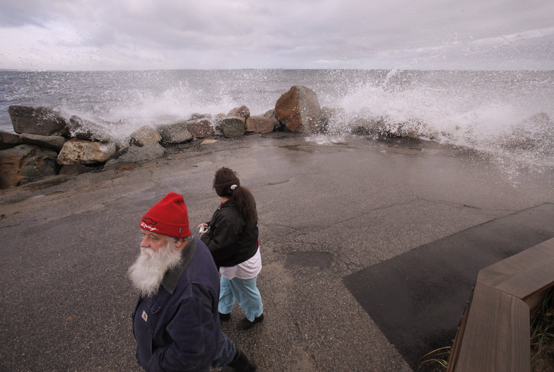 Marcel and Lori Morin of Saco walk down Eastern Avenue in Camp Ellis as water sprays over a sea wall Monday. Damage in southern Maine was said to be widespread, but minor.