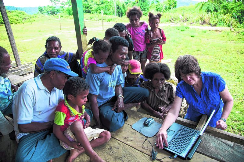 Mandowen, seated at center with his daughter’s arms around his neck, joins fellow villagers on a remote island in Indonesia to watch Linda Jones, right, demonstrate how to transmit Bible translations in their language.