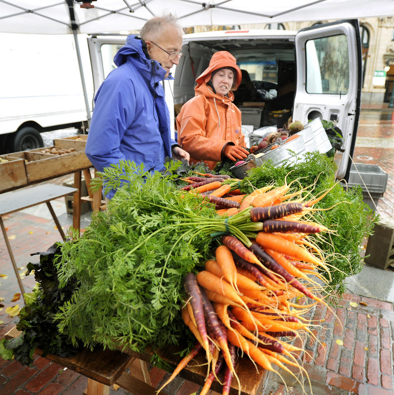 Jeff Brown of Portland buys produce from Mary Ellen Chadd at her Green Spark Farmstand in Monument Square in Portland this month. Growers donated more than 200,000 pounds of their harvests to food pantries, shelters and other charitable groups this year.