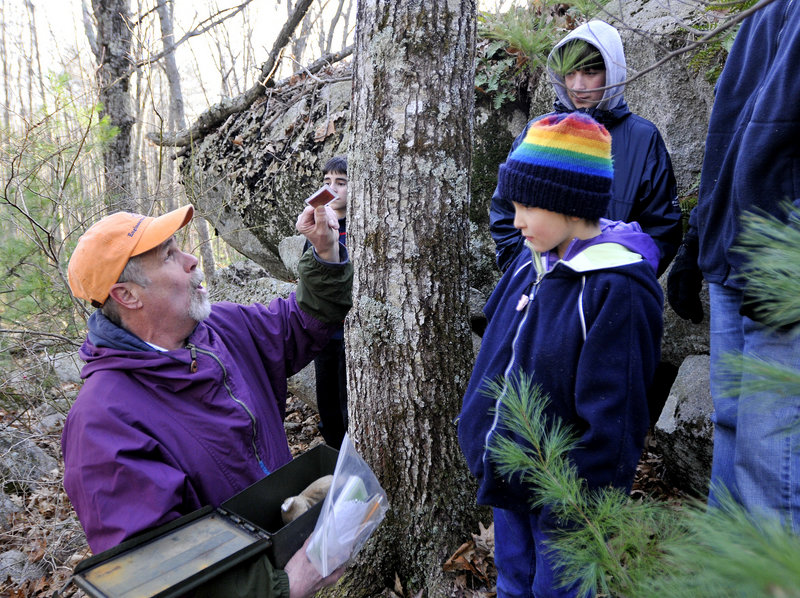 Paul Gadbois shows Gaia Ayres, 8, of Saco and others in the group a coin they found in a geocache during a walk through the sanctuary in Biddeford on Sunday.