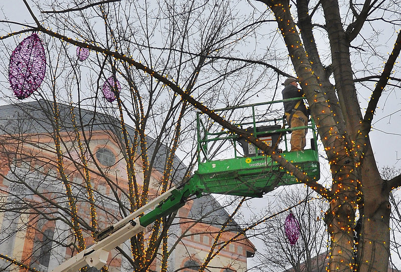 Jesse LaCasse uses a lift to get high into the trees of Tommy’s Park in Portland’s Old Port to install lights designed by his aunt, Pandora LaCasse. He lights the decorations while he works to get a better idea of how they will look.