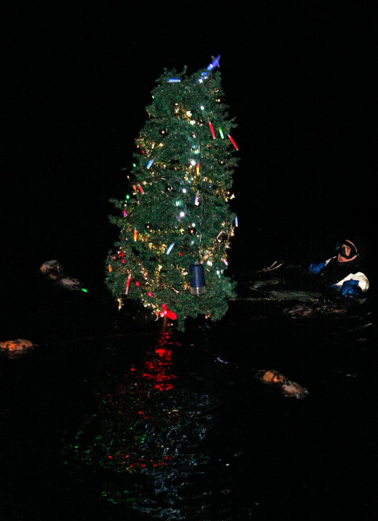 A diver from United Divers of New Hampshire presents a lit tree from under the water at the Lighting of the Nubble ceremony.