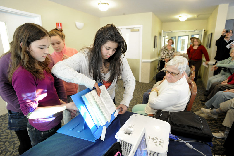 Moore Middle School students from Portland visit residents at the Inn at Village Square in Gorham on Monday to present the residents with adaptive devices for reading and drinking. Julia Martin and Andrea Castro show resident Alice Nicol a book holder.