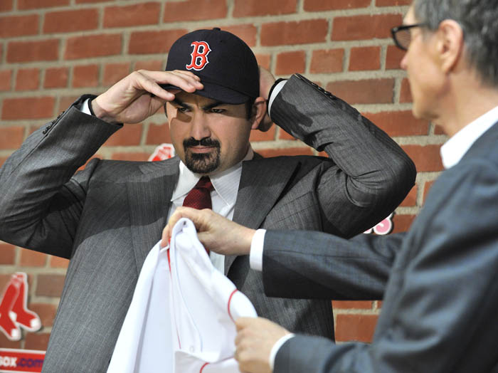New Boston Red Sox first baseman Adrian Gonzalez pulls on his team cap as team owner John Henry holds out his new jersey during a news conference today at Fenway Park.