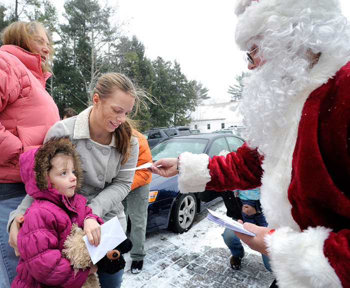 The Secret Santa paid a visit to The Warming Hut in Sebago to give away $100 bills during his first statewide visit today. He is seen here handing out two envelopes to 4-year-old Elana Labrecque and her mother Erica Labrecque.