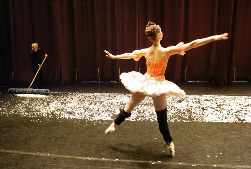 Kate Hamilton warms up on the stage during intermission while Lynn Gilbreath sweeps up confetti from the snowflakes scene that ends Act I of "The Nutcracker" on Saturday. Hamilton dances the role of the Sugar Plum Fairy.