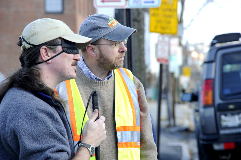 Reporter Ray Routhier, right, waits at a street corner with Wayne Lawson of Portland, who is learning how to navigate sidewalks and streets with the help of a cane. Lawson, whose visual impairment can vary, is wearing a sleep mask to simulate blindness.
