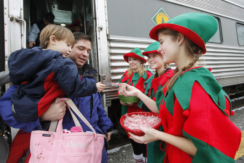 Caiden Chase, 2, of Topsham, with his dad Brett, receives a candy cane from Liz Edgerton after the train ride. The other two elves are Nikki Wadlington and Julia Edgerton.