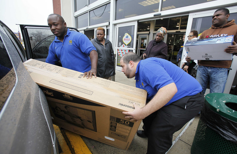Two employees at a Best Buy in Boston help customers load a television into a car. The nation’s largest electronics chain said its quarterly net income fell as it lost sales of laptops and televisions to competitors.