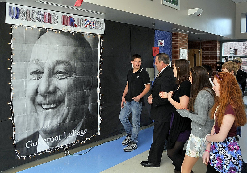Sam Luebbert, left, leads Paul LePage to a computer-generated photo on a welcome wall at Lyman Moore Middle School. He asked LePage to sign the photo and write a message.