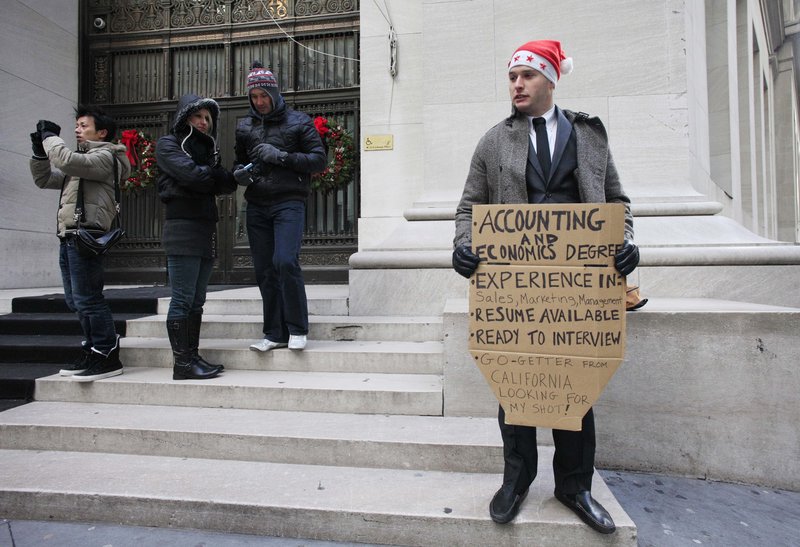 Jesse Paloger holds up a job-seeking sign Wednesday on Wall Street; the bottom of his sign reads, “Go-getter from California looking for my shot!” Last week, initial claims for unemployment benefits dropped for the third time in four weeks.
