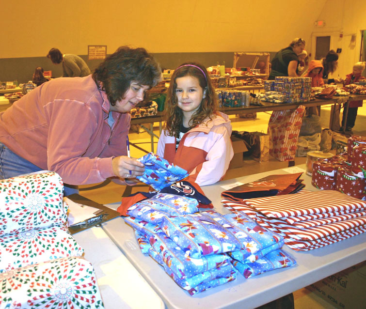 Hollis Parent Teacher Organization volunteer Hope Meserve helps kindergarten student Abbey Cole pick out a present at the school's annual student gift-buying day.