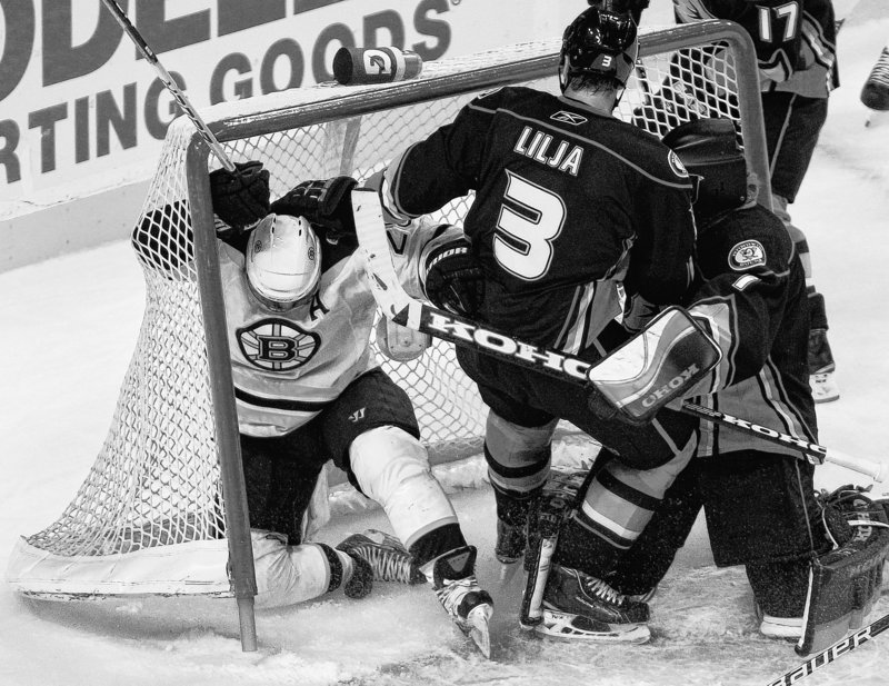 Mark Recchi, left, of the Bruins slides into the goal while chasing the puck ahead of Ducks defenseman Andreas Lilja during Monday night’s game at Boston. Despite outshooting the Ducks in every period, the Bruins suffered a 3-0 loss.