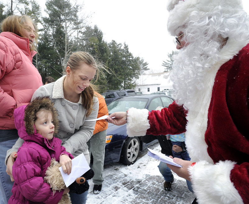Secret Santa's helper hands envelopes to Elana Labrecque, 4, and her mother, Erica Labrecque of Sebago. “This will help us out so much” to have a real Christmas, Erica Labrecque said.