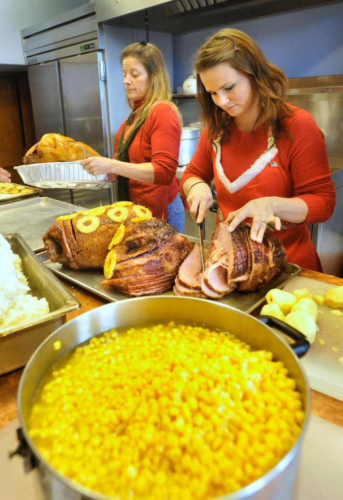 Wendy Rand slices hams in preparation for the meal while Lisa Myrick brings a turkey to the counter.