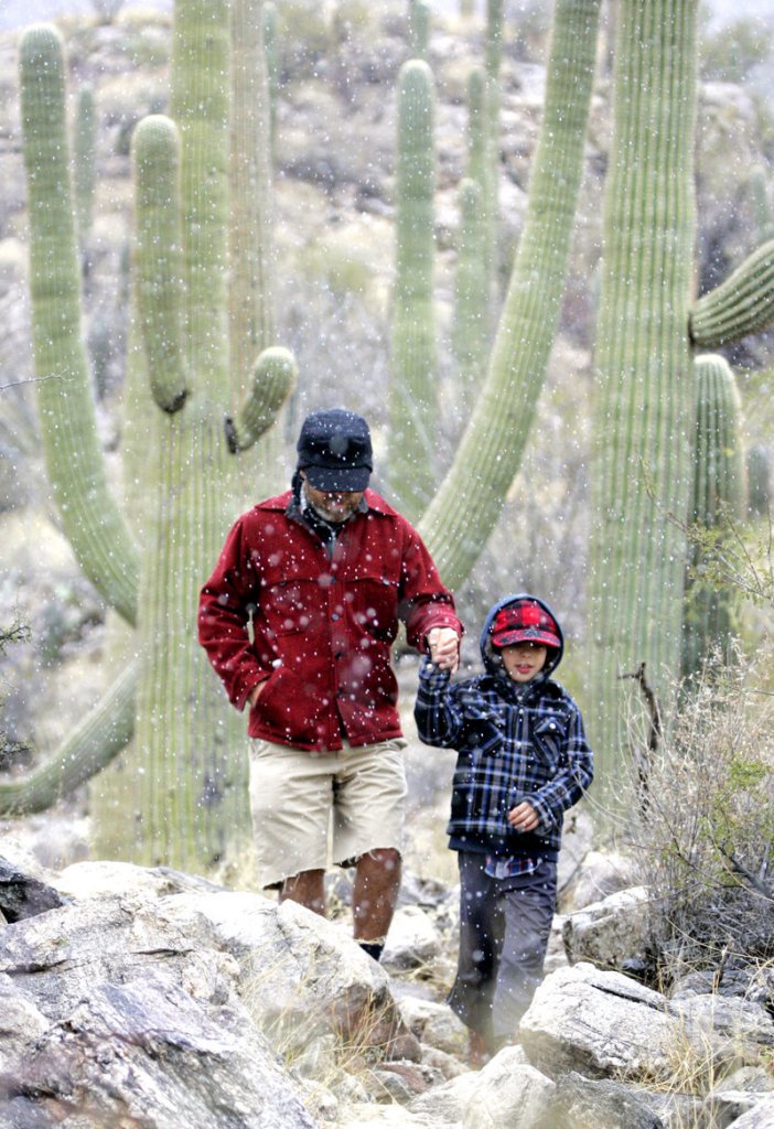 Jon Benjamin, left, walks through snow flurries with his son Judah Benjamin, 7, on the Finger Rock Trail near Tucson, Ariz., on Thursday. The National Weather Service issued a blizzard warning for eastern and southeastern Arizona.