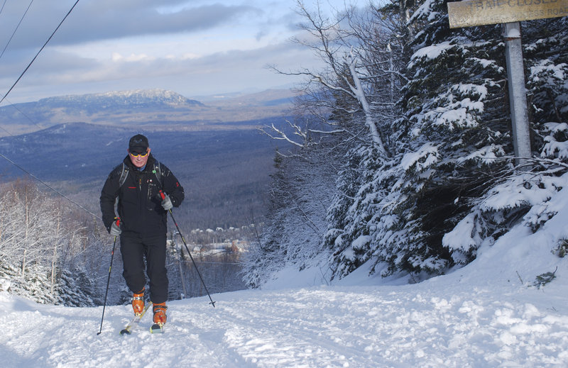 Warren Cook of Kingfield ascends an access road at Sugarloaf recently, with Bigelow Mountain in the background, wearing skis with Alpine touring bindings and skins. Cook, a former ski area owner and manager, has helped give this type of skiing, also called randonnee, a resurgence in Maine.