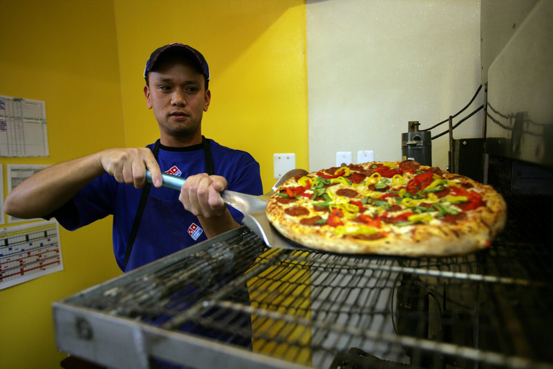 West Lopez of Farmington Hills, Mich., takes a chicken pineapple pizza from the oven at Domino’s Pizza there.