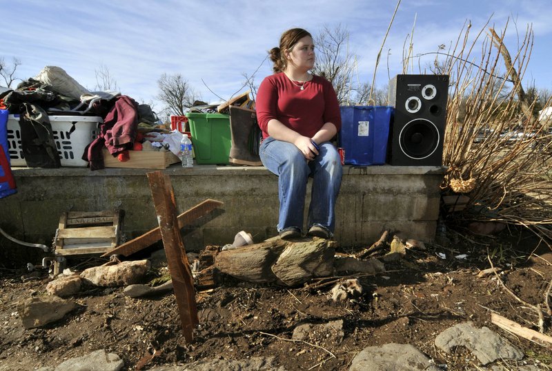 Paige Sisemore, 18, sits on the foundation of a home behind a makeshift cross made from debris after a tornado tore through the small town of Cincinnati, Ark., on Friday. The storm killed three people in Arkansas while three more people died in Missouri.
