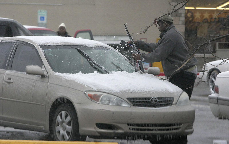 A motorist uses a snow scraper to clean sleet and ice from his windshield and wiper blades in El Dorado, Ark., on Sunday, after a winter storm dumped a mix of sleet and snow on the area.