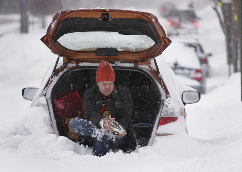 Josh Denkmore of Portland changes his shoes to get ready to dig out his car on Cumberland Avenue amid Wednesday’s snowstorm.