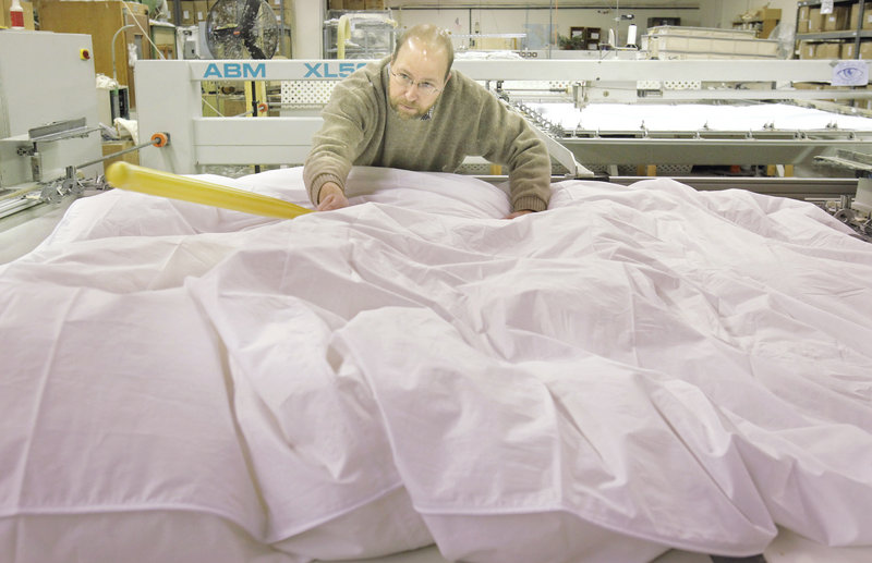 Using a plastic baseball bat, Ray Routhier spreads the stuffing in a down comforter before it is sewn at Cuddledown in Portland.