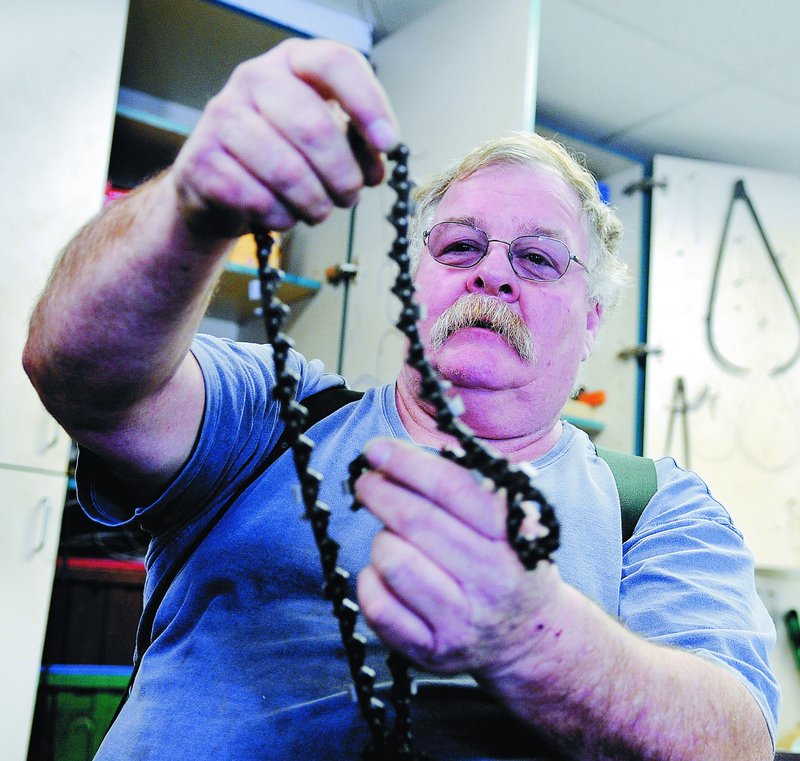 David Lancaster unfurls a chain for a saw Sunday at his South China workshop.