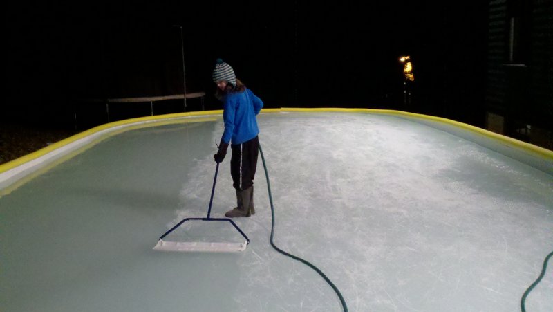 Michael Roy’s daughter, Eliza, uses a hand-held mini-Zamboni to smooth the ice on their backyard rink in Camden.