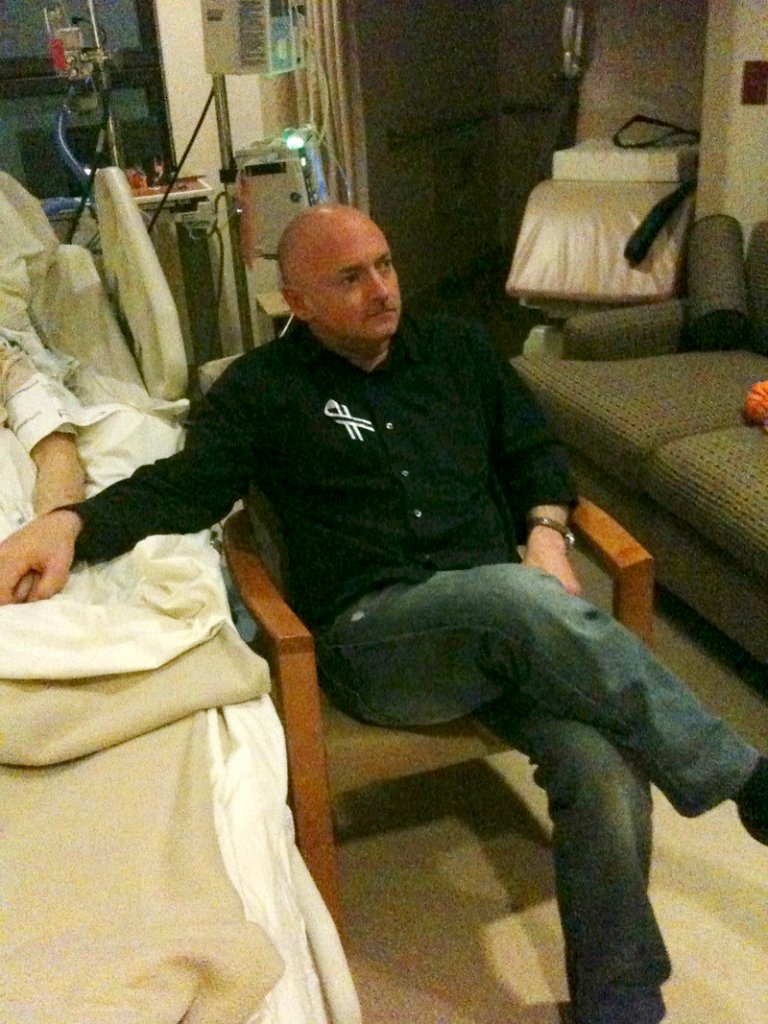 A photo released by the office of U.S. Rep. Gabrielle Giffords shows Giffords’ husband, Mark Kelly, holding his wife’s hand as he watches the State of the Union address Tuesday night.