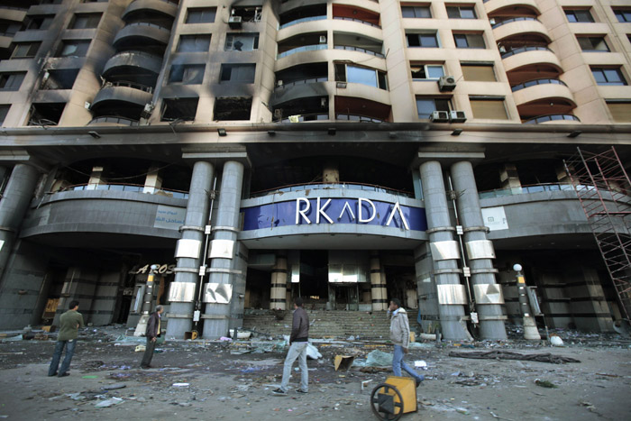 Egyptians walk past Cairo's Arcadia shopping center, which was looted and set on fire recently. The protests engulfing Cairo have shuttered businesses, forced factories to stop operating, closed banks and the stock exchange and limited suppliers' ability to restock store shelves.