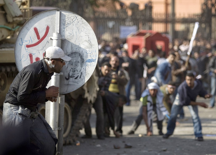 An anti-government protester shelters behind a road sign as pro-government demonstrators throw rocks in Cairo today.