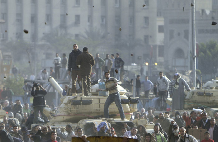 Stones fly through the air as supporters of President Hosni Mubarak, foreground, fight with anti-Mubarak protesters, rear, standing on army tanks in Cairo.