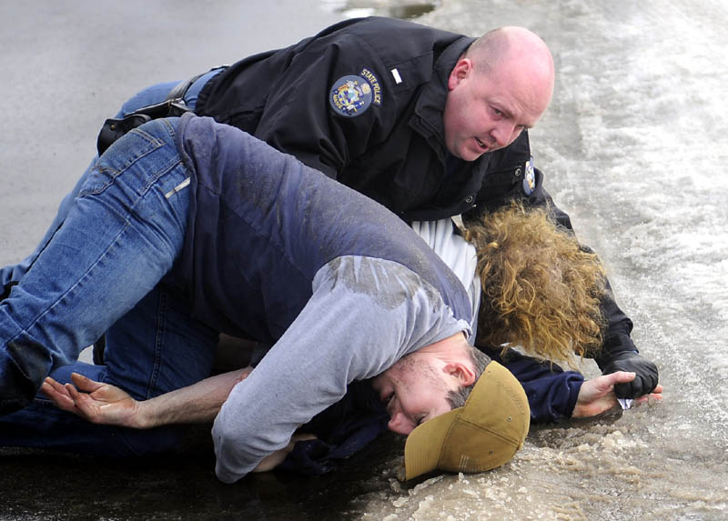 Off-duty state police trooper Jon Leach, left, wrestles Jerry Larravee, center, to the ground with State Police Lt. Brian Scott Monday in Manchester. Leach, who is on sick leave following shoulder surgery, disarmed Larravee, 47, after he pulled a knife after driving in the wrong lane of traffic, according to police.