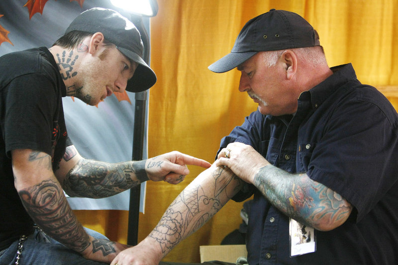 Dave Buchanan, right, of Portland and artist James McGrory of Fianna Studio in Portland discuss a design on Buchanan’s arm during an annual tattoo show in South Portland on Sunday. “If someone says it doesn’t hurt, they’re lying,” said Buchanan, a tollbooth worker who serves as a daily advertisement for McGrory when he reaches out to take money.