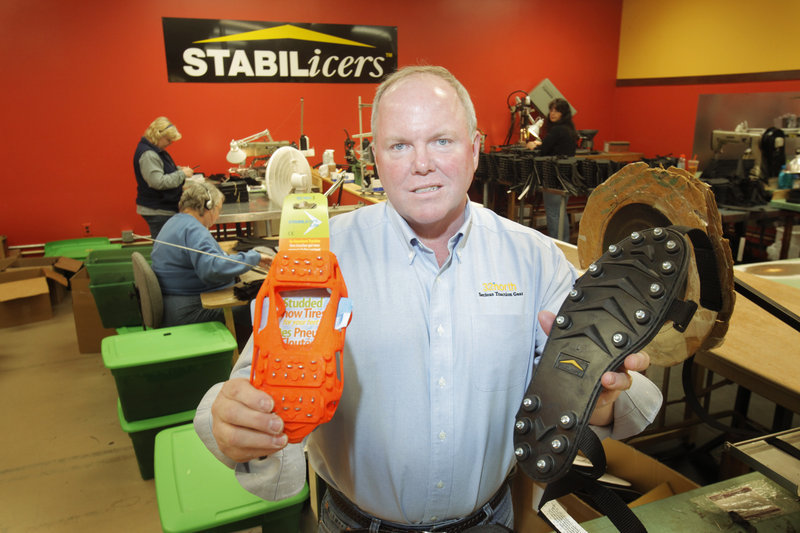 Doug Norton, president of 32north in Biddeford, holds a pair of the original STABILicers traction footwear, right, and STABILicers Light, both of which are worn over shoes to improve traction on ice and snow.