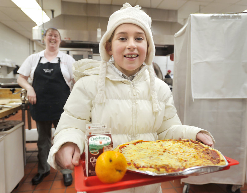 Grace Murphy, 10, a fifth-grader at Wentworth Intermediate School in Scarborough, carries a gluten-free pizza made by kitchen manager Leslie Dumais. Grace has celiac disease, a condition in which eating gluten damages the interior of the small intestine.
