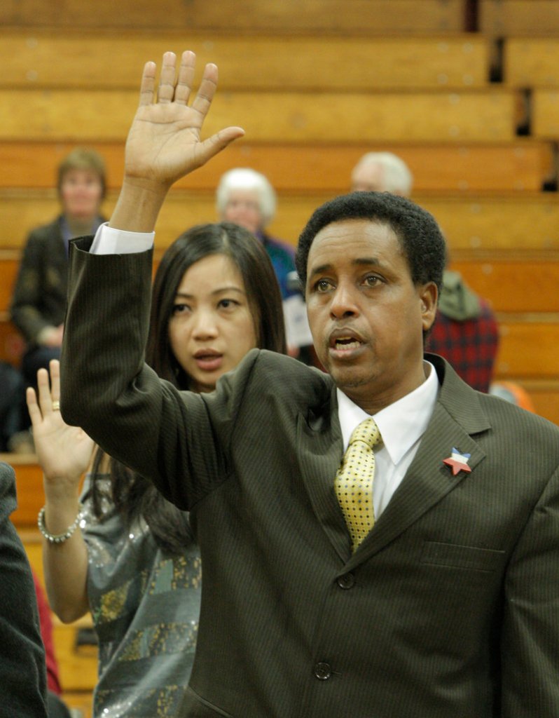 Abdulahi Abdi holds his hand high while being sworn in as a new U.S. citizen on Thursday in Falmouth.