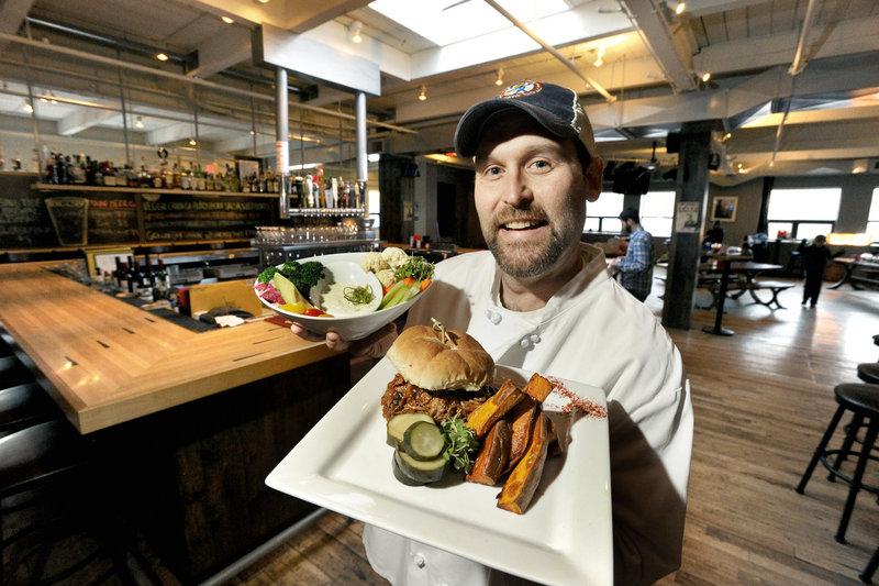 Chef James Turner displays a veggie dip and a pulled pork sandwich at Bayside Bowl in Portland. The restaurant has been open since June.