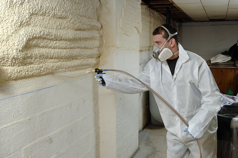 Jim Boilard, a weatherization tech for Weatherize Northeast, sprays foam on basement walls at a Yarmouth home under a program offered by the Maine Housing Authority.