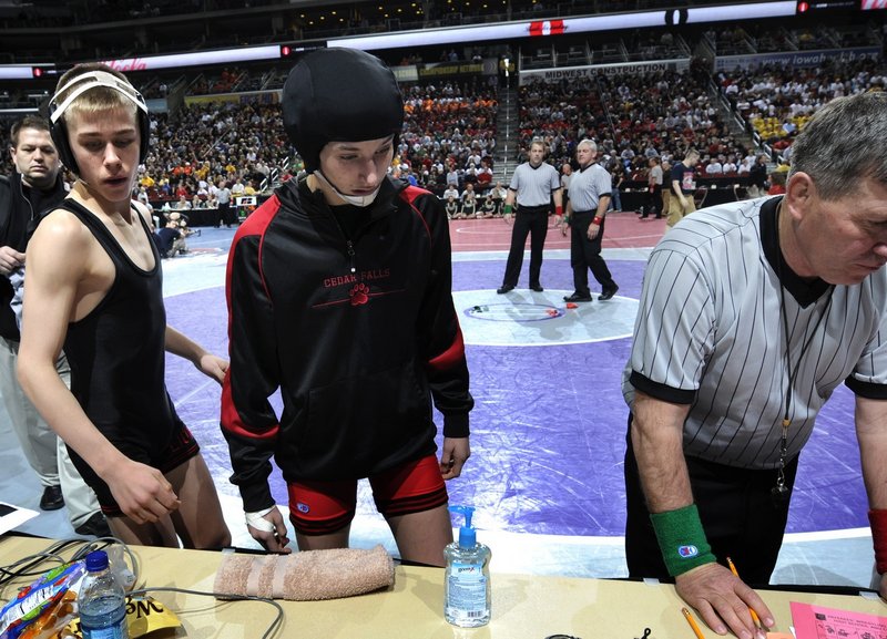 Cedar Falls’ Cassy Herkelman, center, and her opponent Joel Northrup, left, of Linn-Mar High, wait for their leg bands before their match at the Iowa state wrestling tournament Feb. 17 in Des Moines. Northrup forfeited rather than face a girl.