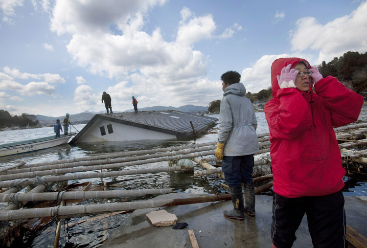 Reiko Kikuta, right, and her husband Takeshi Kikuta watch as workers attempt to attach ropes to their submerged home to try to pull it ashore with construction equipment on Oshima Island in northeastern Japan today. 9.0 Magnitude Earthquake; Destruction; Devastation; Disaster; Ea