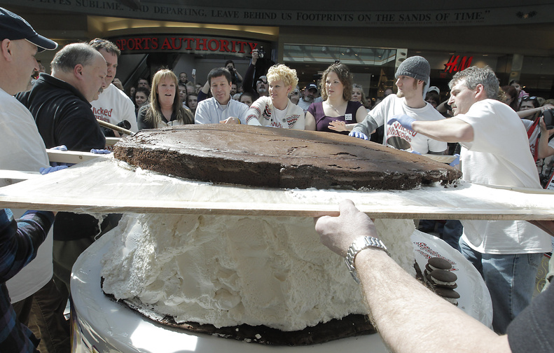 Amy Bouchard, fourth from right, owner of Wicked Whoopies, gets some help putting the 180-pound devil’s-food cake top on the 1,067-pound whoopie pie that was assembled at the Maine Mall in South Portland on Saturday. Radio station WMGX and Gardiner-based Wicked Whoopies joined forces to create a pie that would surpass Pennsylvania’s 250-pound confection.