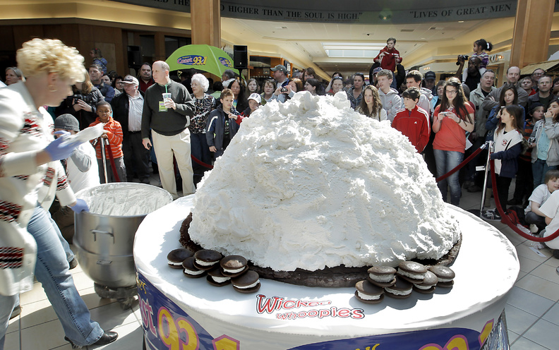 Amy Bouchard, owner of Wicked Whoopies, far left, puts the final dollops of filling on the over the 1,067-pound whoopie pie before adding the top devil's food layer at the Maine Mall in South Portland today. Competing with Pennsylvania's 250-pound pie, Maine is looking to make the whoopie pie the state's official treat.