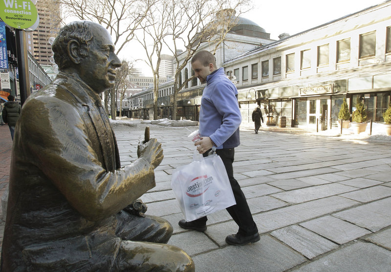 A shopper walks past a bronze sculpture of famed Boston Celtics coach Red Auerbach at Qunicy Market in downtown Boston recently. Consumers bought more from retailers for a seventh straight month in January. But snowstorms limited the spending gains expected from workers with more money in their paychecks from a Social Security tax cut.