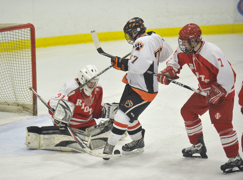 Stephen Comar of Biddeford tries to kick loose a rebound while Biddeford goalie Dominic Desjardins attempts to cover the puck.